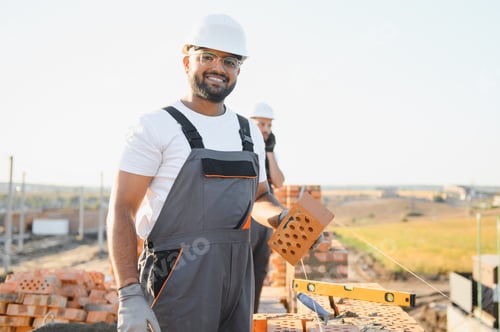 Preview: A team of Indian construction workers in overalls and hard hats are building a brick wall