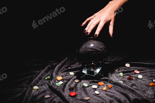 Preview: cropped view of fortuneteller hand above crystal ball with fortune telling stones on black velvet