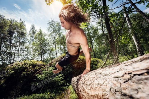 Preview: Young man jumping over a tree trunk in the forest.