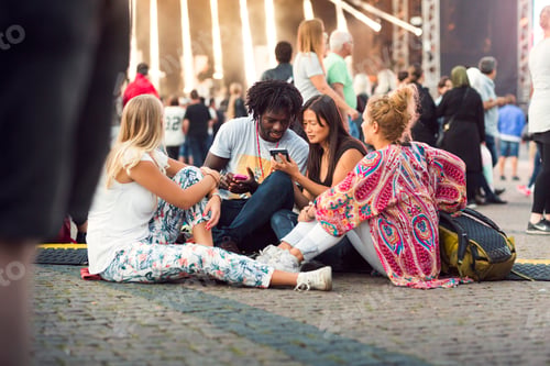 Preview: Friends sitting on ground watching smartphone at music concert