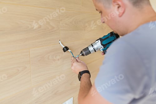 Preview: Young caucasian man doing home repairs, using a screwdriver he installs electric lights