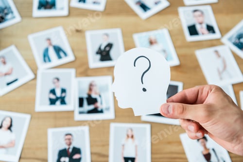 Preview: cropped view of man holding paper with human head and question mark near photos