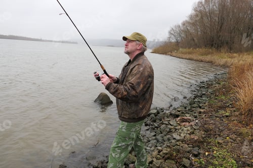 Preview: A fisherman, a man catches fish with a fishing rod, from the bank of the river.