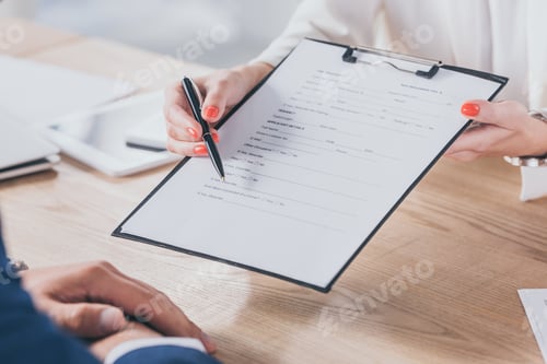 Preview: cropped view of businesswoman pointing with hand at signature place in agreement while sitting near
