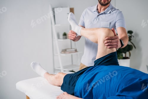 Preview: partial view of rehabilitation therapist massaging senior mans leg on massage table