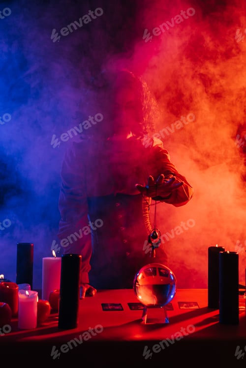 Preview: fortune teller holding amulet near crystal ball and candles near colorful smoke on foreground
