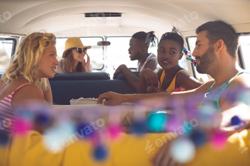 Preview: Front view of happy group of diverse friends talking with each other in a camper van at beach