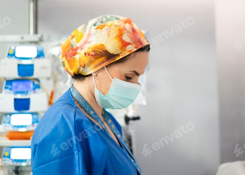 Preview: Female doctor wearing surgical mask and colorful scrubs cap working in hospital room