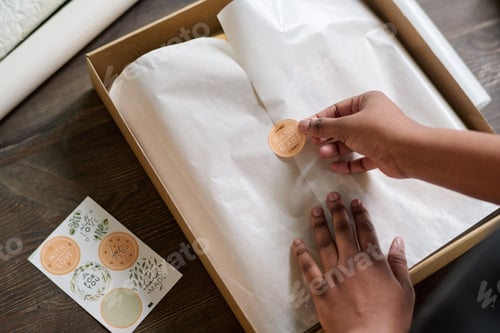 Preview: Hands of female worker of warehouse putting sticker on top of wrapping paper