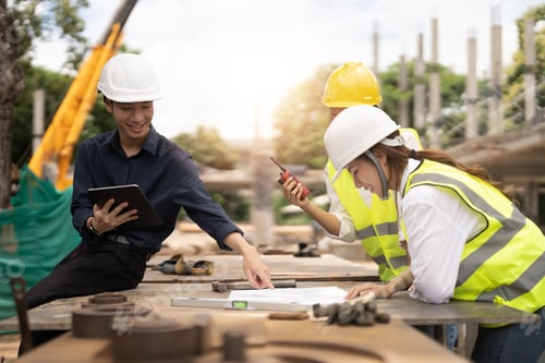 Preview: Young asian architects and engineer discussing blueprints at construction site