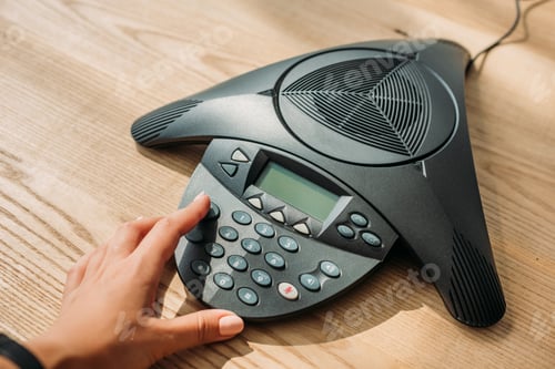 Preview: cropped shot of businesswoman with pink nails pushing button of speakerphone at workplace