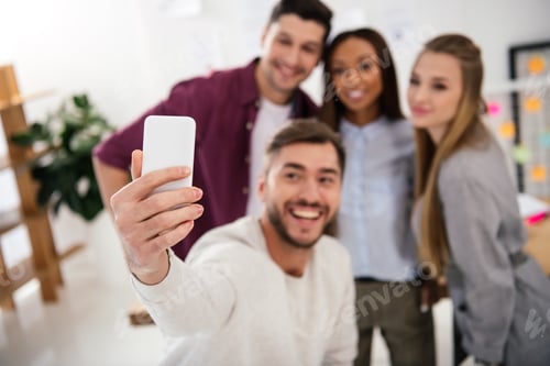 Preview: selective focus of happy multicultural business people taking selfie on smartphone together in