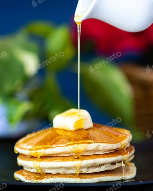 Preview: Vertical shot of pouring honey on hotcakes with a butter pat on top