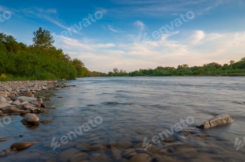Preview: Landscape with trees, stones, blue sky with puffy white clouds and a river with smooth water in
