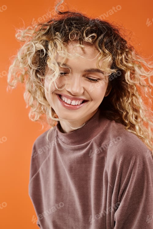 Preview: portrait of charming smiling woman with wavy hair in brown turtleneck on radiant orange background