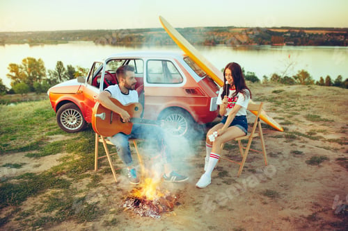 Preview: Couple sitting and resting on the beach playing guitar on a summer day near river