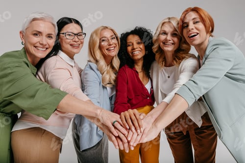 Preview: Multi-ethnic group of happy mature women holding hands together against grey background