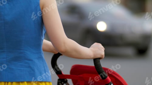 Preview: Young mother walking with baby carriage at the street back view close up. Mother with a stroller