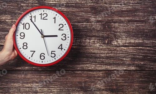Preview: Hand holding clock on wooden background.