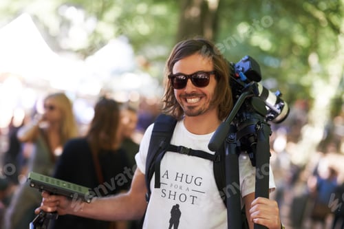 Preview: A smiling photographer carrying camera and tripod at a music festival