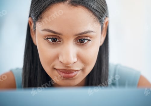 Preview: Happy young mixed race businesswoman focused while working on a laptop alone in an office at work.