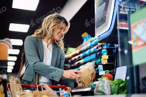 Preview: Happy woman paying for groceries at cash register in supermarket.