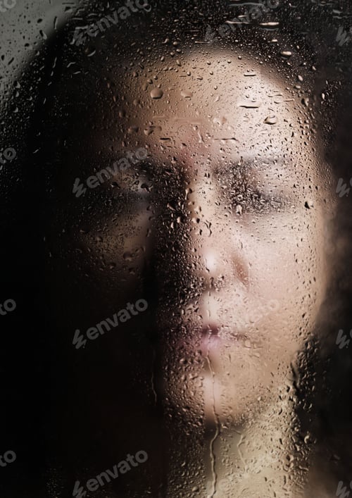 Preview: a woman's face through the glass on a rainy day