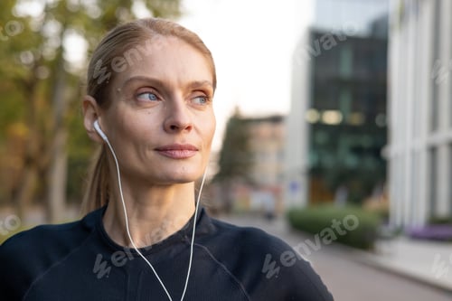 Preview: Focused woman jogging in the city with earphones enjoying a fitness routine
