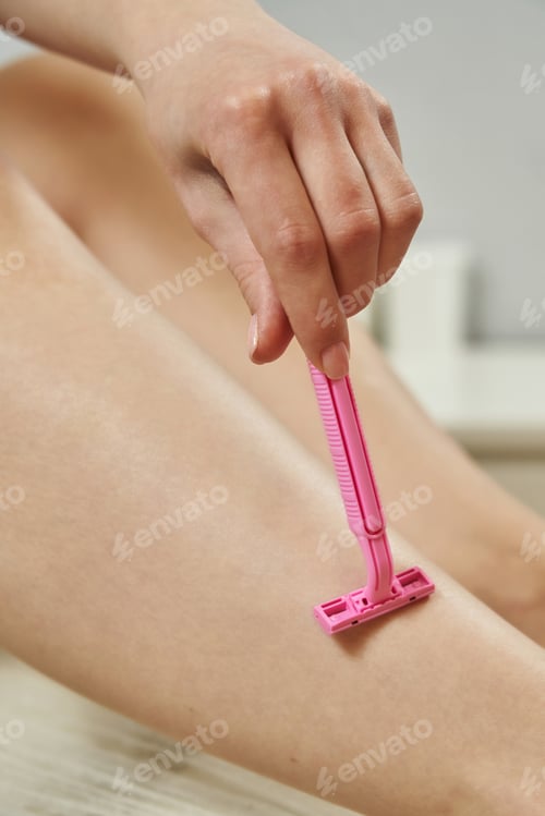 Preview: a female hand runs a pink female razor over the smooth skin of a female leg