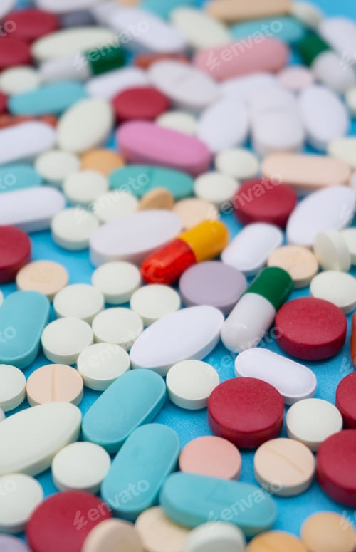 Preview: Vertical shot of colorful pills of different shapes on a blue background