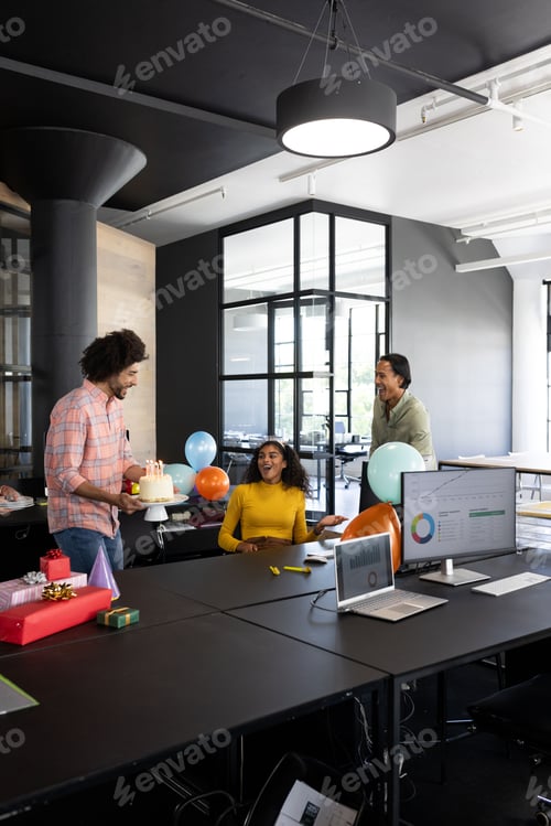 Preview: In office, colleagues celebrating birthday with cake and balloons, smiling happily