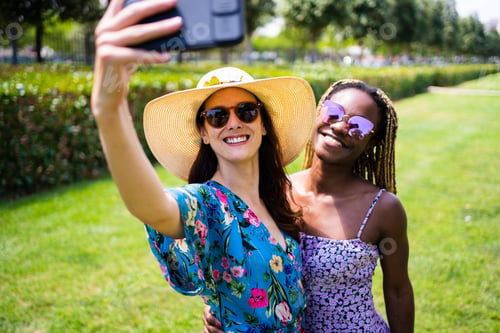 Preview: Two multiethnic women smiling while taking a selfie outdoors