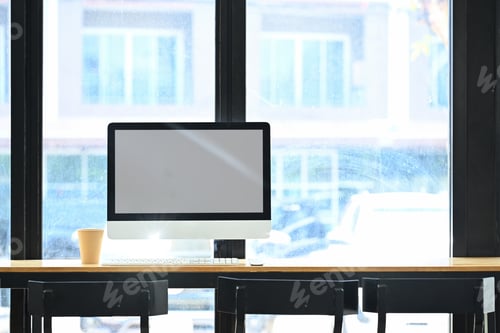 Preview: Front view of blank computer monitor and paper cup of coffee on wooden table