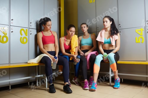 Women in Fitness Gear Sit on Locker Bench