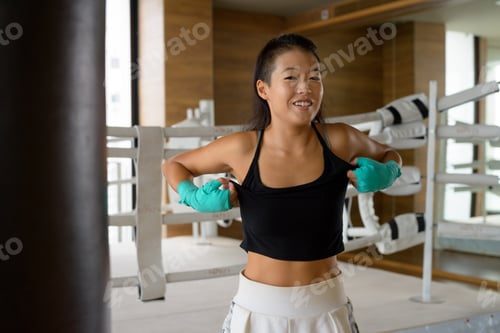 Preview: Asian woman kick boxer looking happy and smiling while ready for exercise at gym