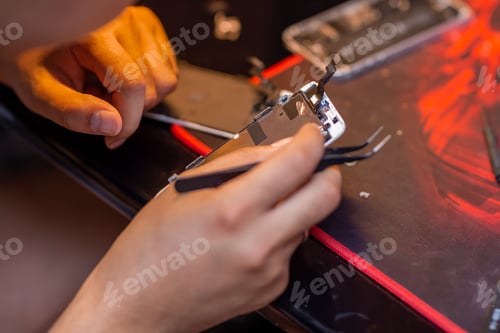 Preview: A man is repairing a mobile phone. In the frame, his hands and details of the device. repair shop