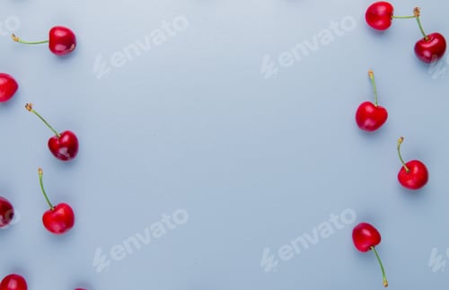 Preview: top view of red cherries on left and right sides and blue background with copy space