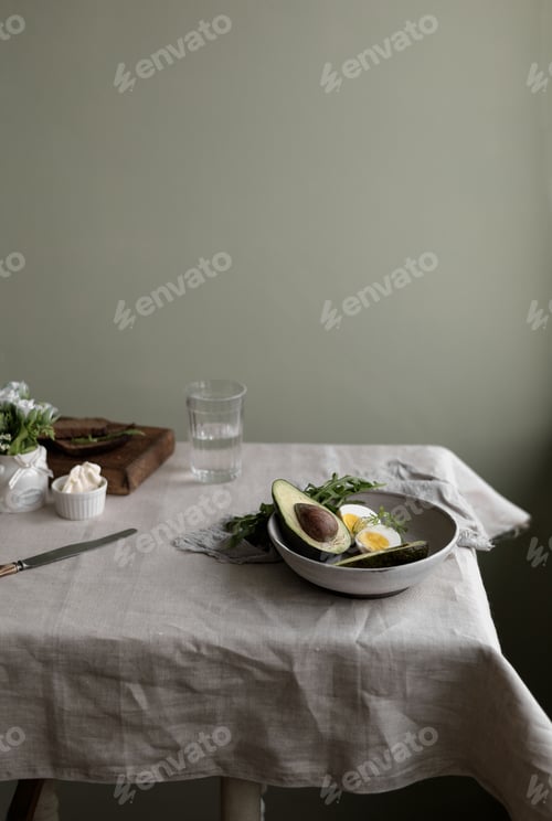 Preview: Healthy food for breakfast - a glass of water, avocado, eggs, fresh herbs in a bowl, bread, cheese.