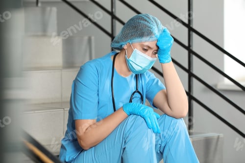Preview: Exhausted doctor sitting on stairs in hospital