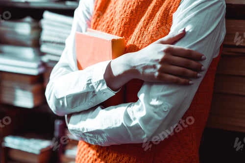 Preview: cropped view of woman with crossed arms holding book in library