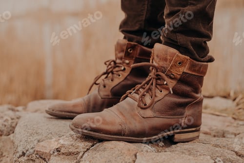 Preview: man in brown old leather boots and trousers stands on stones against blurred background