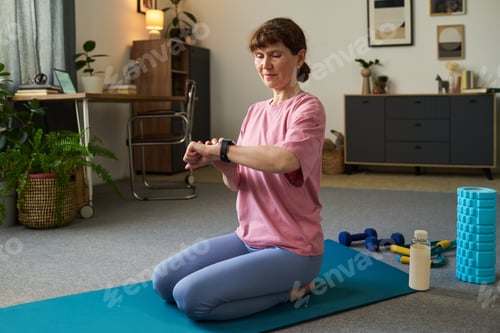 Preview: Senior Caucasian Woman Checking Smartwatch While Practicing Yoga Indoors