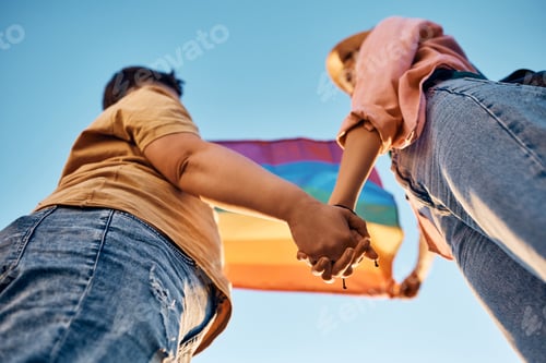Preview: Below view of women holding hands and LGBT flag against the sky.
