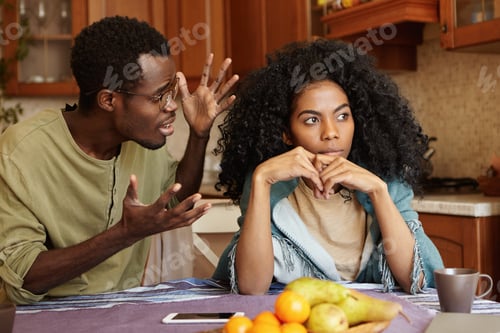 Preview: People and relationships concept. African American couple arguing in kitchen: man in glasses gesturi