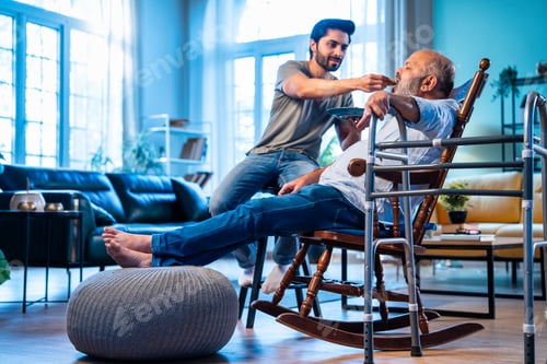 Preview: Indian Devoted young man serving homemade meal to elderly dad in cozy interior.