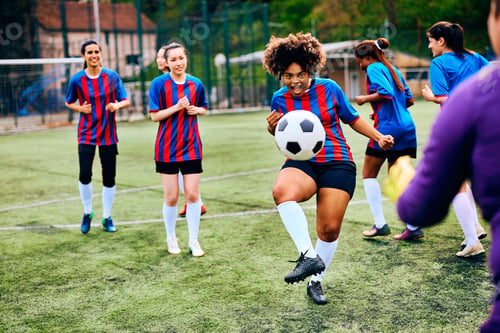 Preview: Black soccer player kicking the ball during practice with her teammates at the stadium.