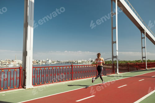 Preview: Woman trains running along road on contemporary footbridge on summer day