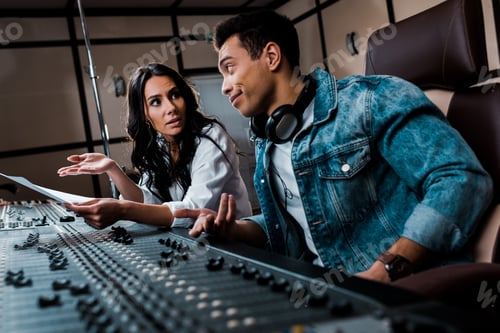 Preview: two quarrelling multicultural sound producers working at mixing console in recording studio