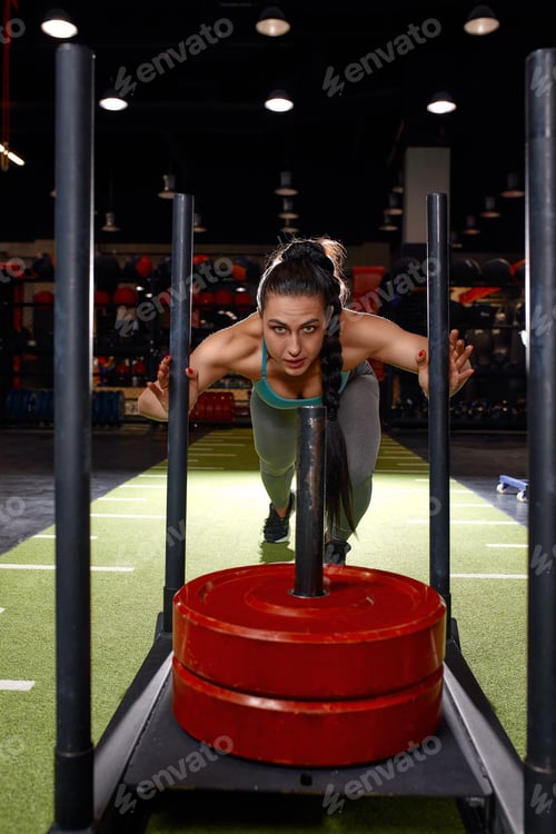Preview: Beautiful young woman with barbell weight plate working out in sports club