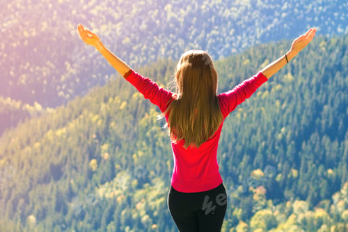 Preview: Silhouette of a young happy beautiful slim girl in red sweater standing on big rocks
